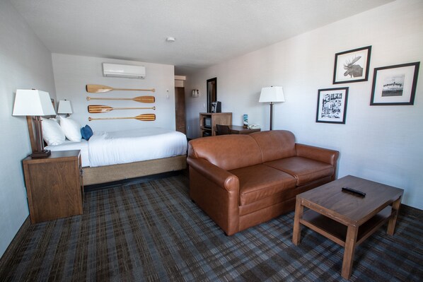 A hotel room with a bed, a brown leather sofa, a small wooden table, and a TV stand.