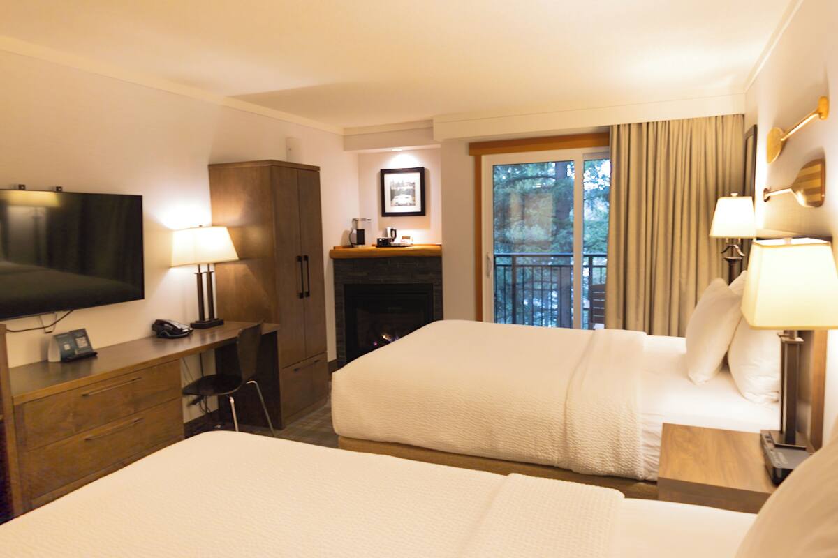 Habitación de hotel con dos camas, un escritorio con computadora, televisor y chimenea.