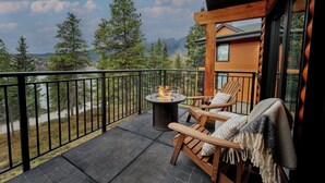 Een balkon met een vuurkuil, houten stoelen en uitzicht op bergen.