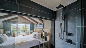 Een slaapkamer met een groot bed, een nachtkastje, een douche en uitzicht op de natuur.