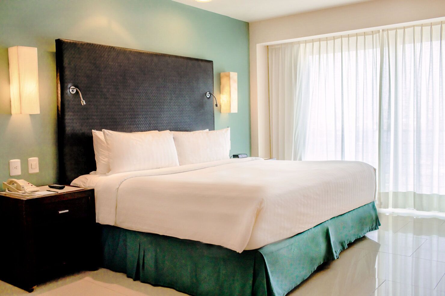 A hotel room with a large bed, a nightstand with a phone, and a window with curtains.