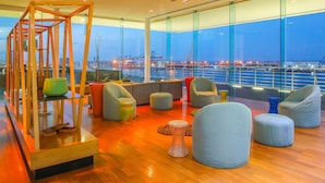 Un salón moderno con estructura de madera, asientos cómodos y vista a un puerto al anochecer.