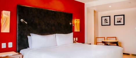 A hotel room with a large bed, a wooden nightstand, a small table, and two framed pictures on the wall.