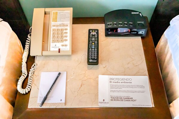 Una habitación de hotel con cama, mesita de noche, control remoto, teléfono y una tarjeta de bienvenida.