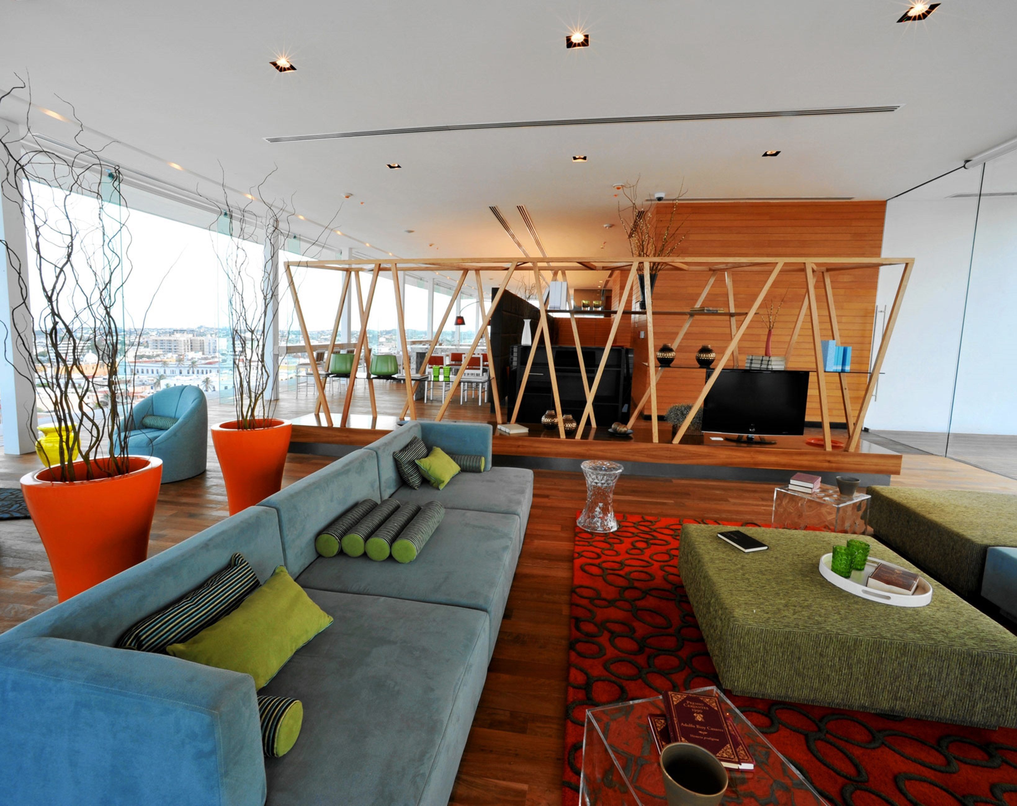 A modern living room with a blue sofa, orange planters, and a red patterned rug.