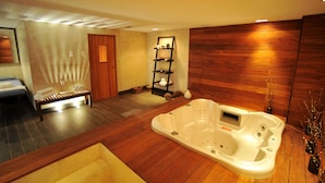 Un cuarto de spa con piso de madera, una camilla de masaje, una bañera blanca y un estante con artículos de tocador.