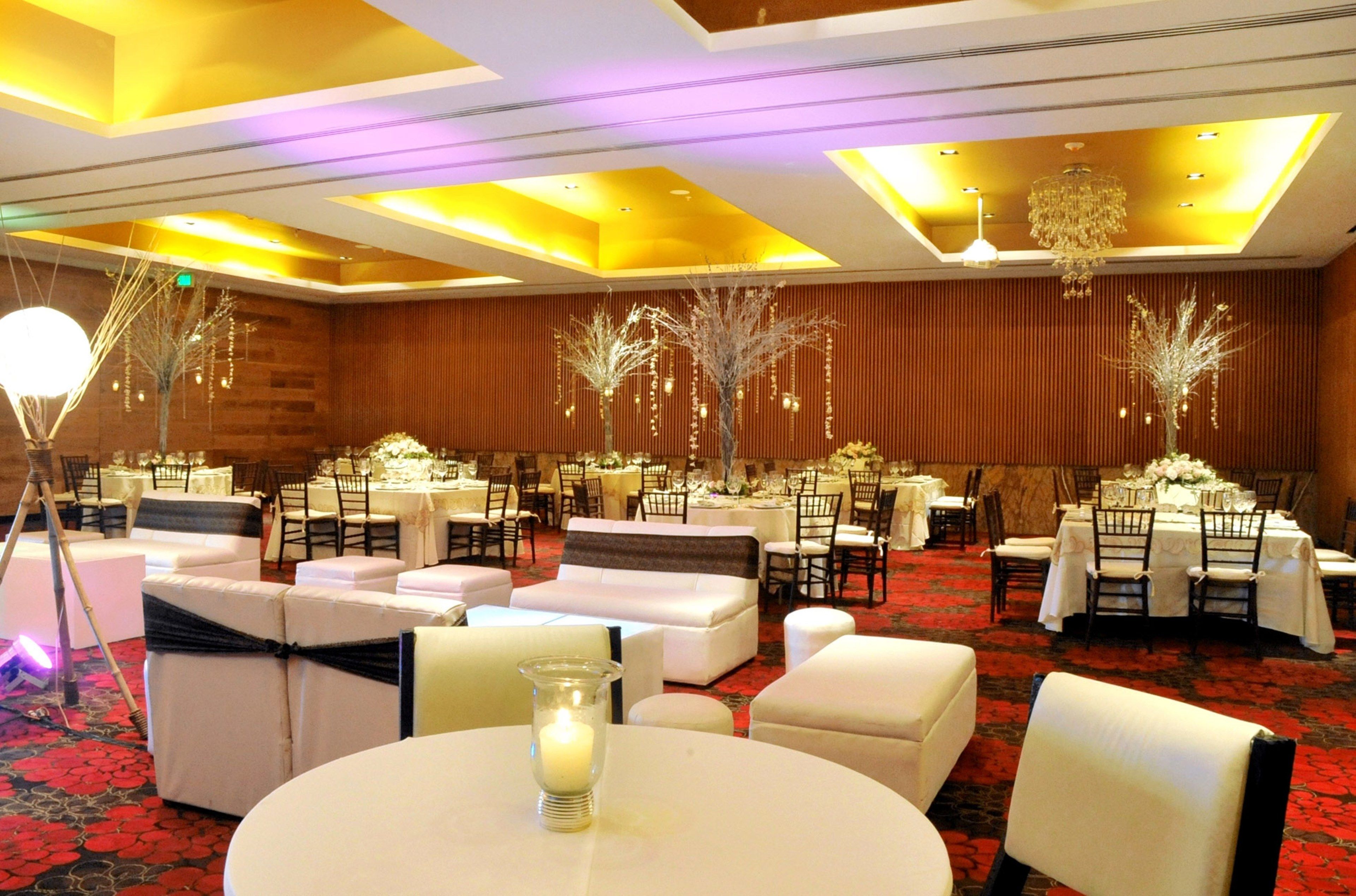 A banquet hall with round tables, white sofas, and chandeliers.