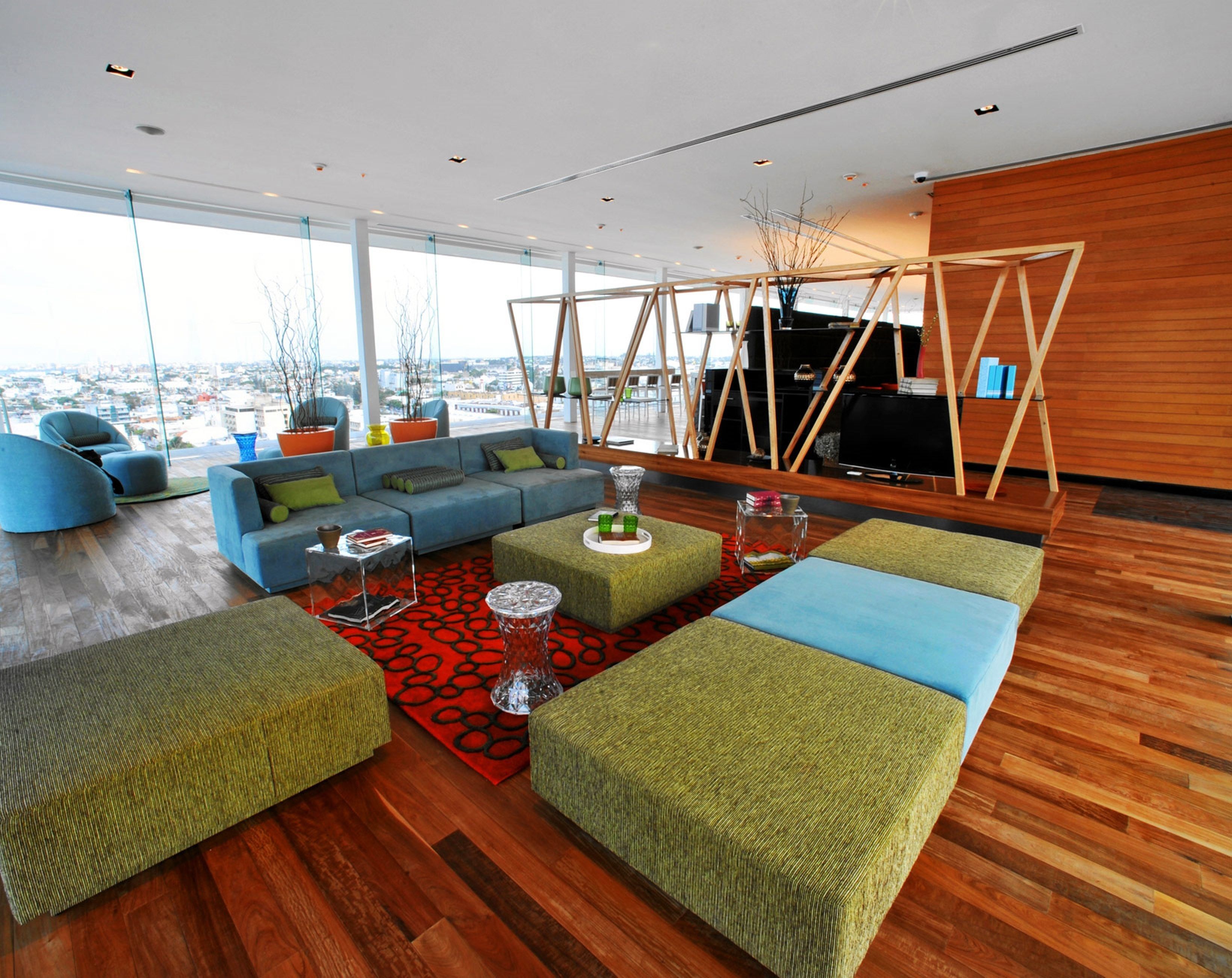 A modern living room with a sofa set, ottomans, and a coffee table. There is a large window offering a view of the city.