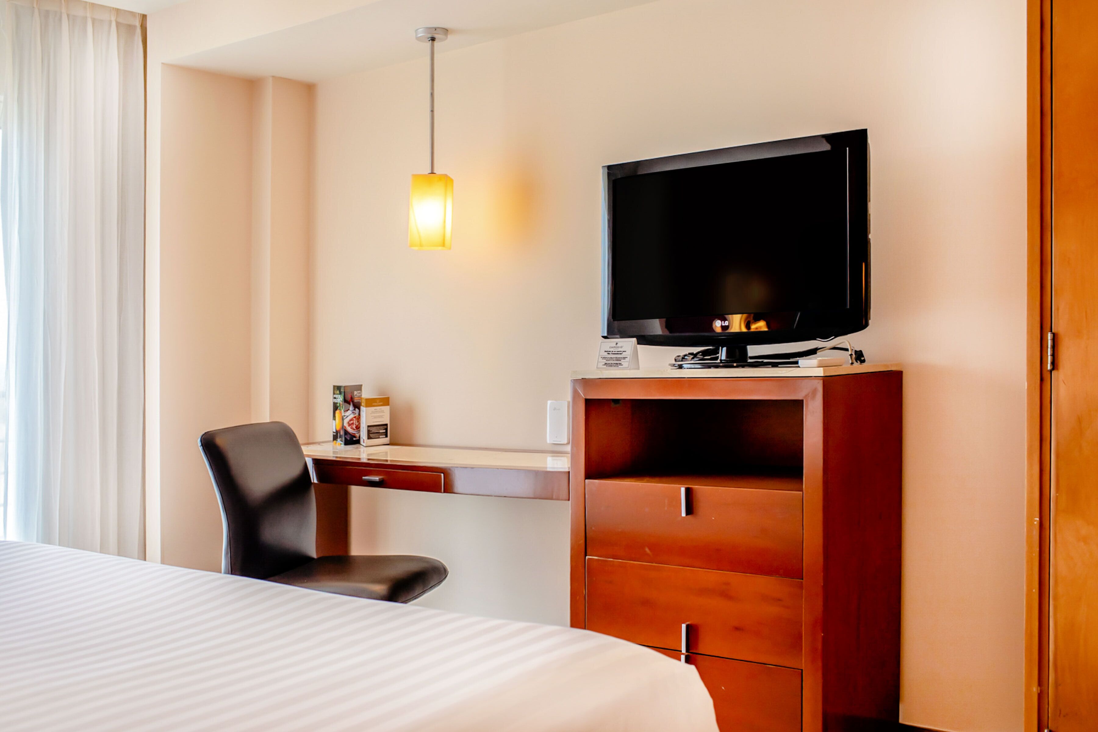 Una camera d'albergo con un letto, una scrivania con televisore, una sedia e un armadio.