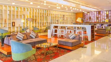 Un moderno vestíbulo de hotel con sofás, sillones, una zona de bar y una estantería.