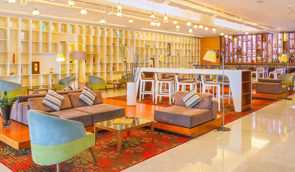 Un moderno vestíbulo de hotel con sofás, sillones, una zona de bar y una estantería.
