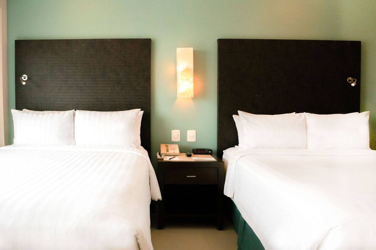 Una habitación de hotel con dos camas, una mesita de noche y una lámpara fijada a la pared.