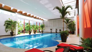 Una piscina interior con sillas de descanso rojas y plantas en macetas.