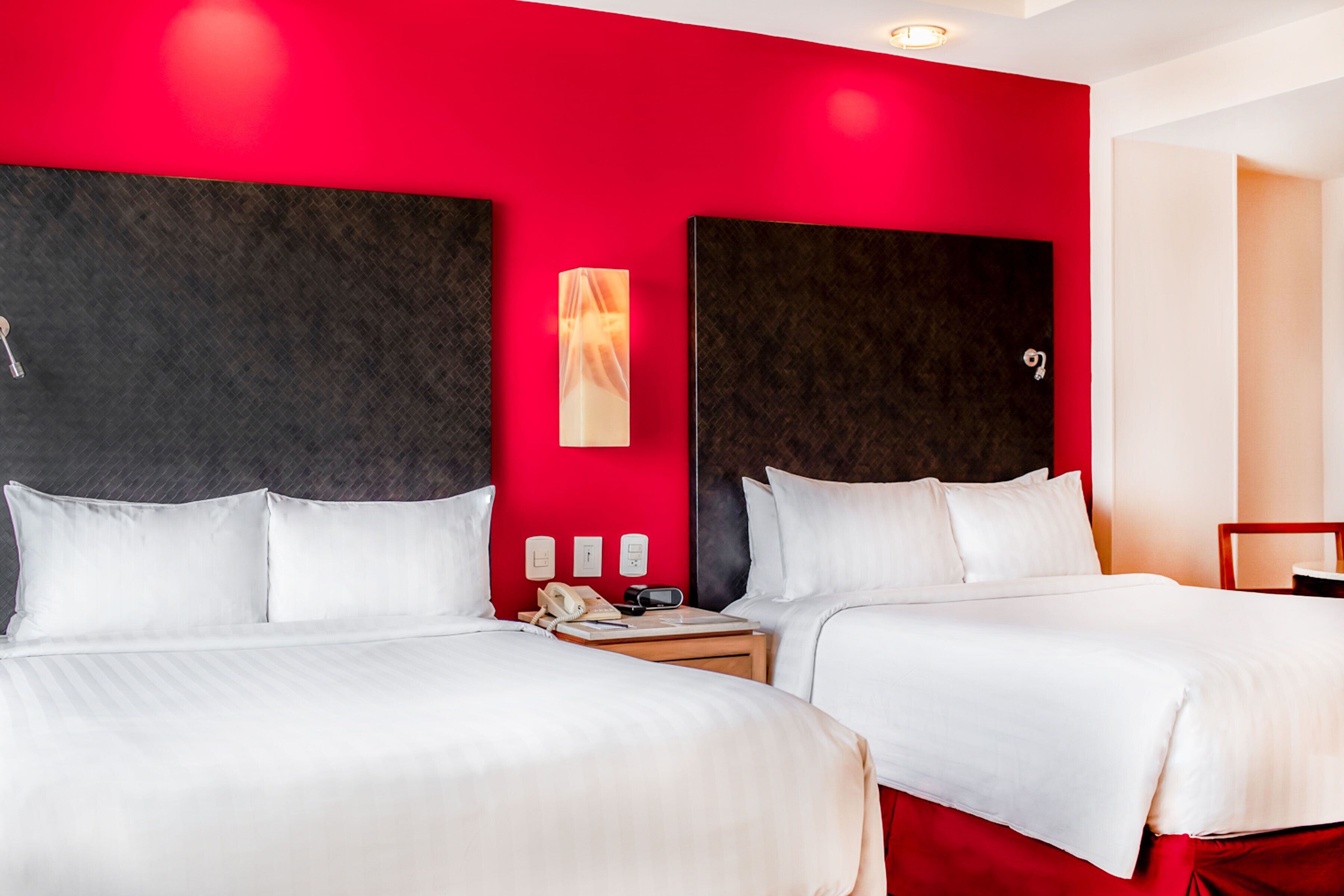 Habitación de hotel con dos camas, una pared de acento roja y diseño moderno.