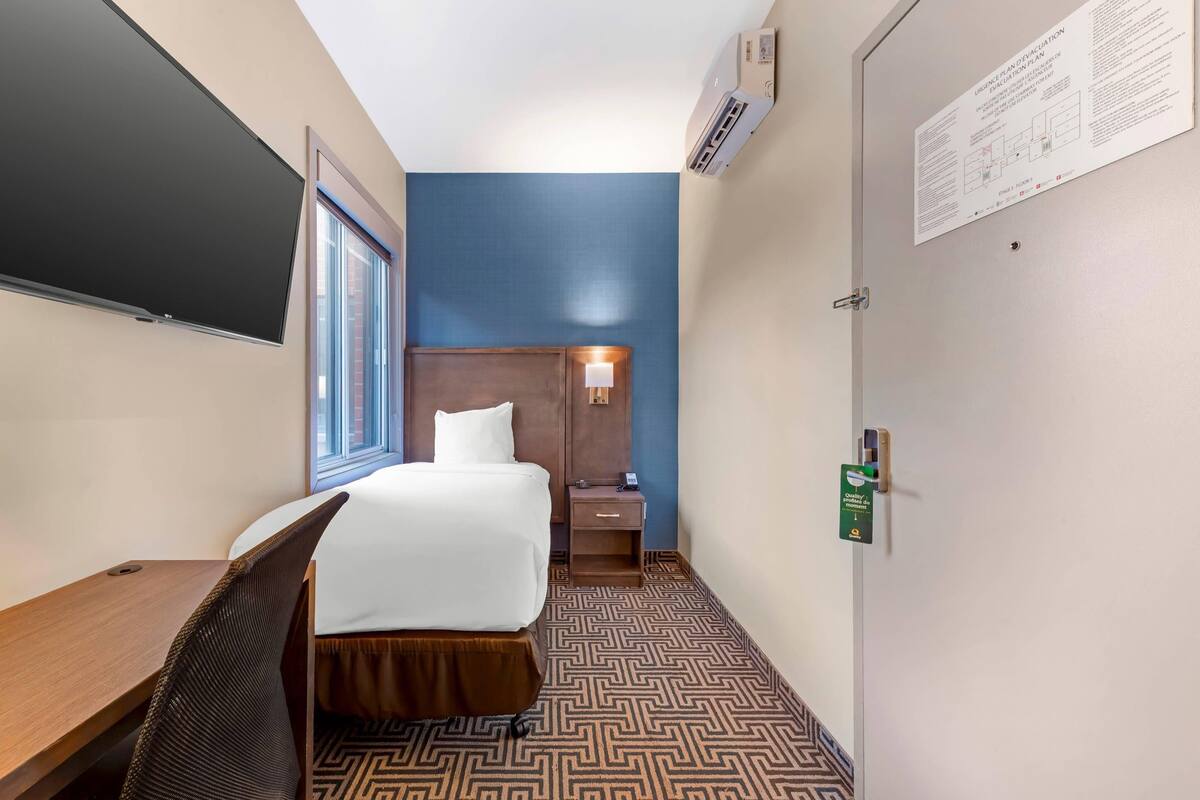 A hotel room with a bed, bedside table, lamp, and a large window.