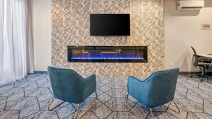 A modern room with a fireplace, a flat-screen TV, and two blue chairs. - Quality Inn Centre-Ville (Montreal)