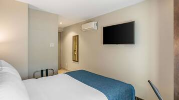 Een hotelkamer met een bed, een flatscreen televisie aan de muur, een airconditioning en een deur naar een andere kamer.