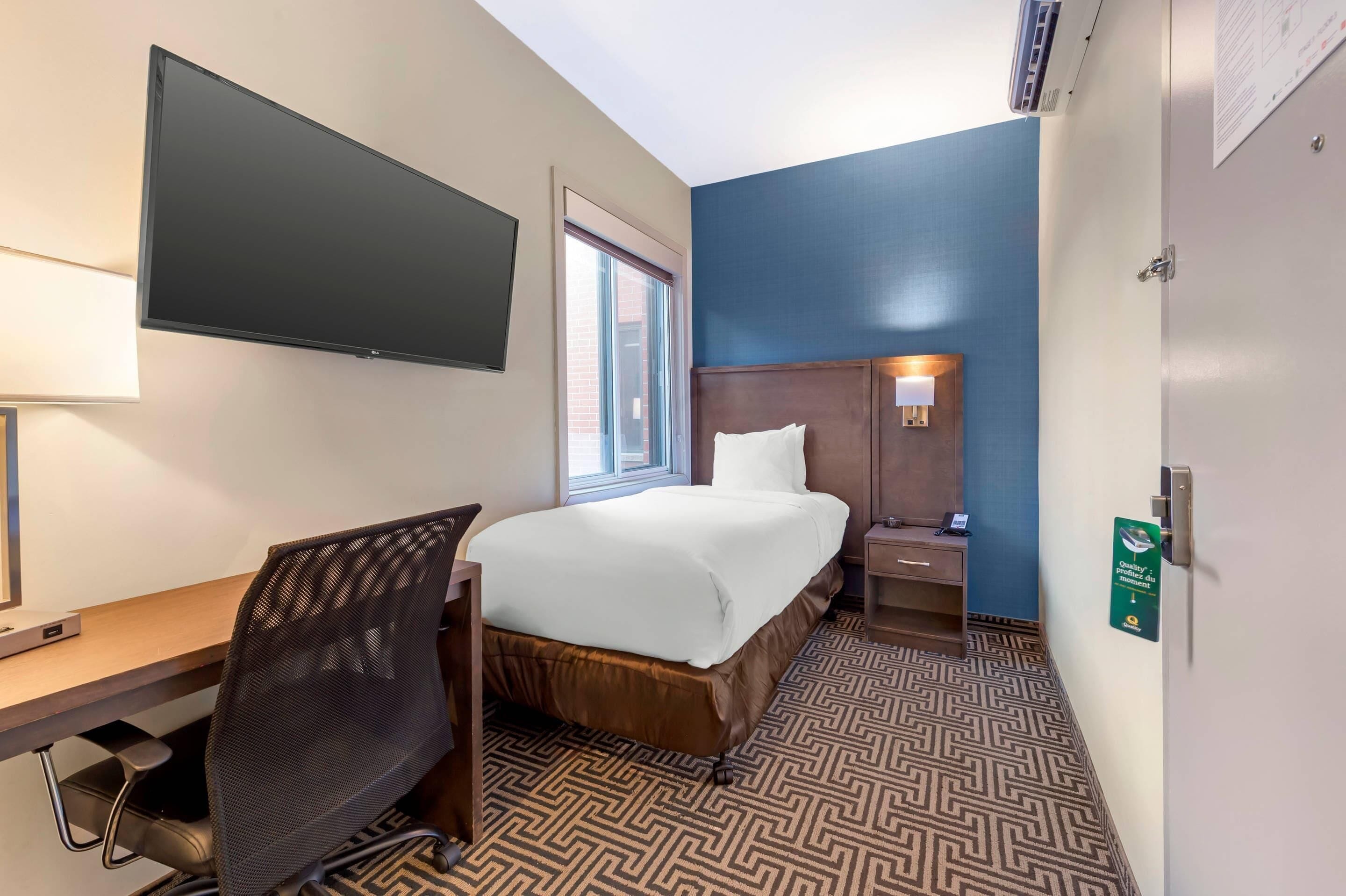 Habitación de hotel con cama, escritorio, silla y televisión de pantalla plana.
