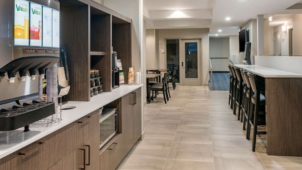 A modern kitchen with a built-in coffee machine, a dining area with a long table and chairs, and a TV mounted on the wall. - Quality Inn Centre-Ville (Montreal)