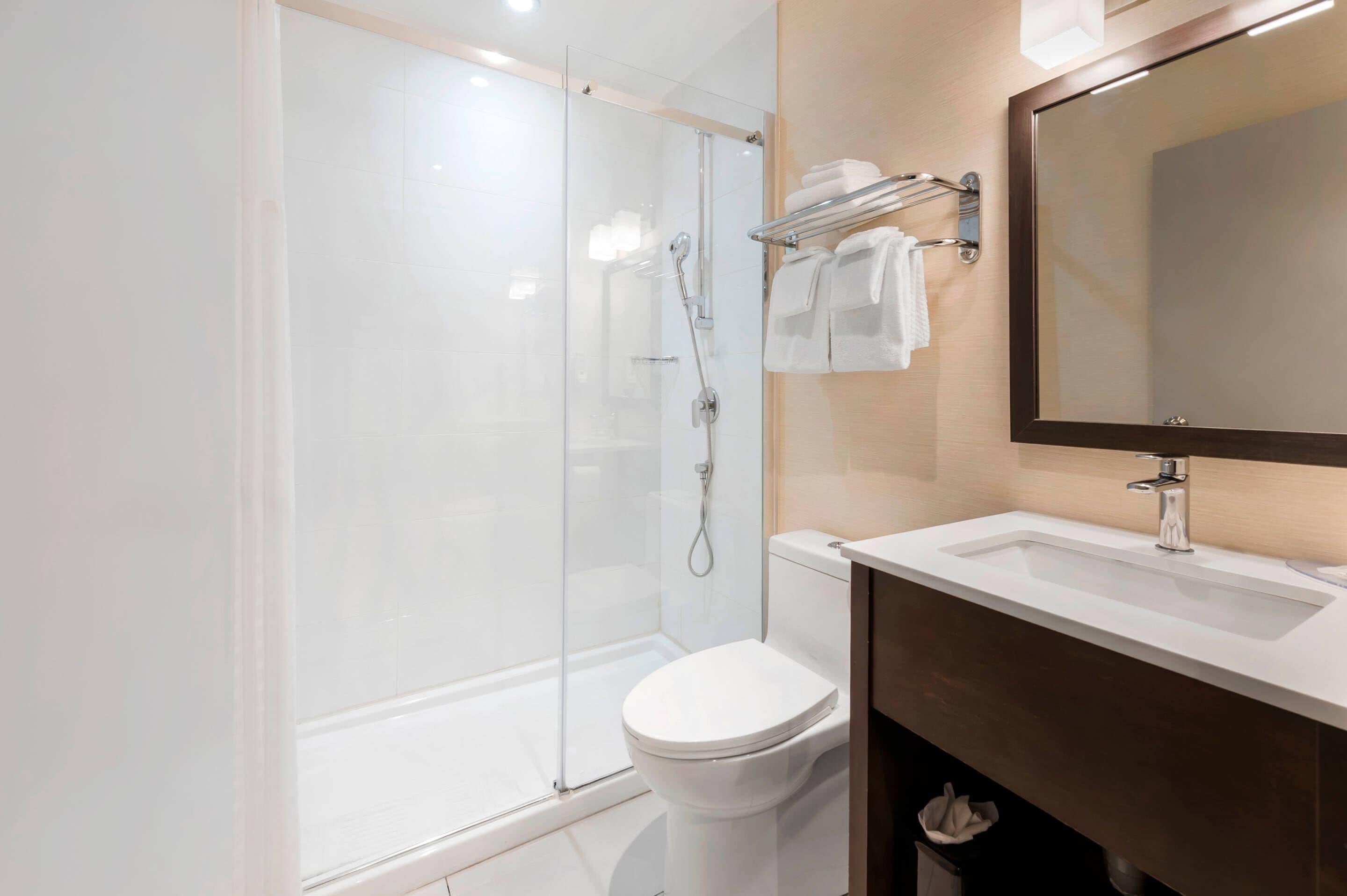 Une salle de bain moderne avec une douche à parois de verre, des toilettes blanches et un meuble-lavabo avec un miroir.