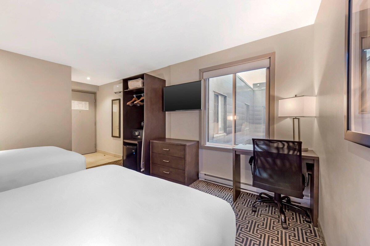 A hotel room with two beds, a desk, a chair, a wardrobe, a TV, and a window with a view.