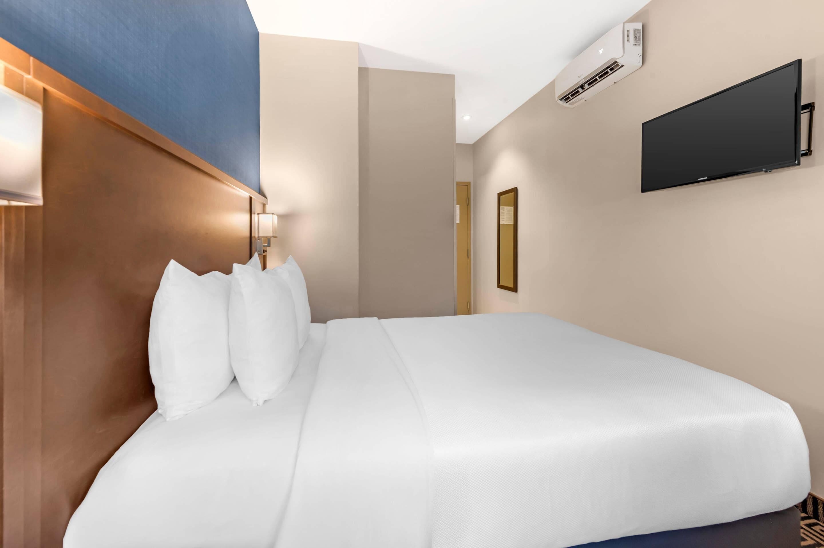 A hotel room with a large bed, a flat-screen TV mounted on the wall, and an air conditioning unit.