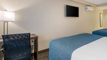Habitación de hotel con escritorio, silla, dos camas, televisor y aire acondicionado.