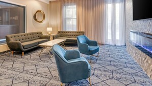 A modern hotel room with a sofa, two armchairs, a coffee table, a TV, and a fireplace. - Quality Inn Centre-Ville (Montreal)