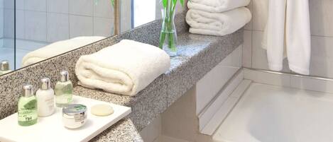 A bathroom with a bathtub, a towel rack, a mirror, and a vanity with toiletries.