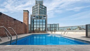 Piscina no terraço com cobertura de vidro e parede de tijolos.