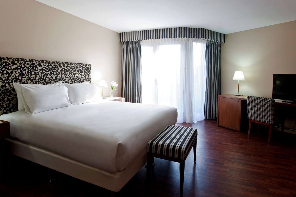 Une chambre d’hôtel avec un grand lit, un bureau, une télévision et une fenêtre avec des rideaux.