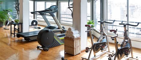 Un gimnasio amplio con diverso equipo de ejercicio, grandes ventanales y suelo de madera.