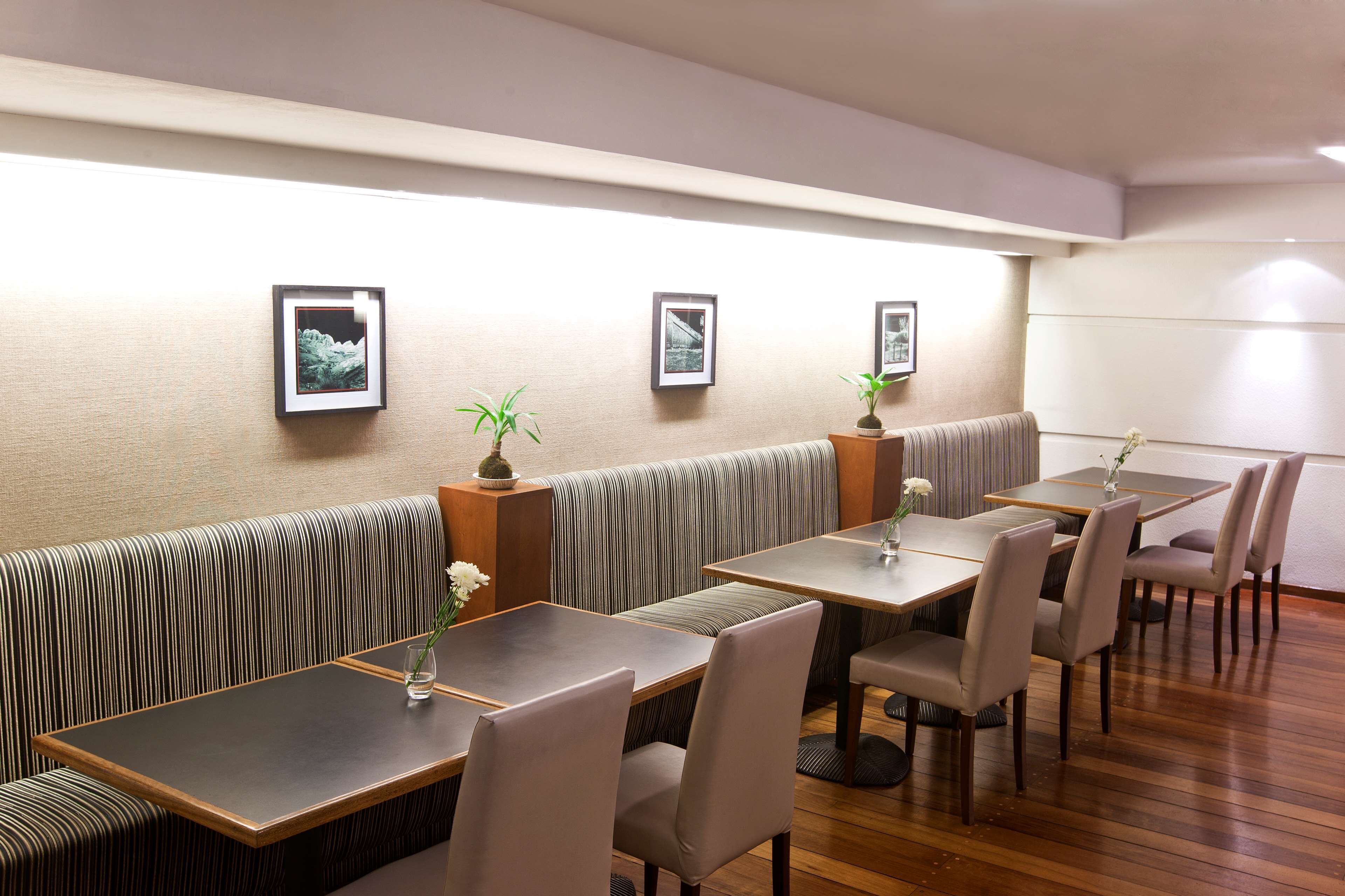 Un restaurante con cabinas y mesas, cuadros en la pared y plantas en macetas.