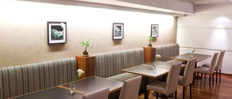 Un restaurante con cabinas y mesas, cuadros en la pared y plantas en macetas.