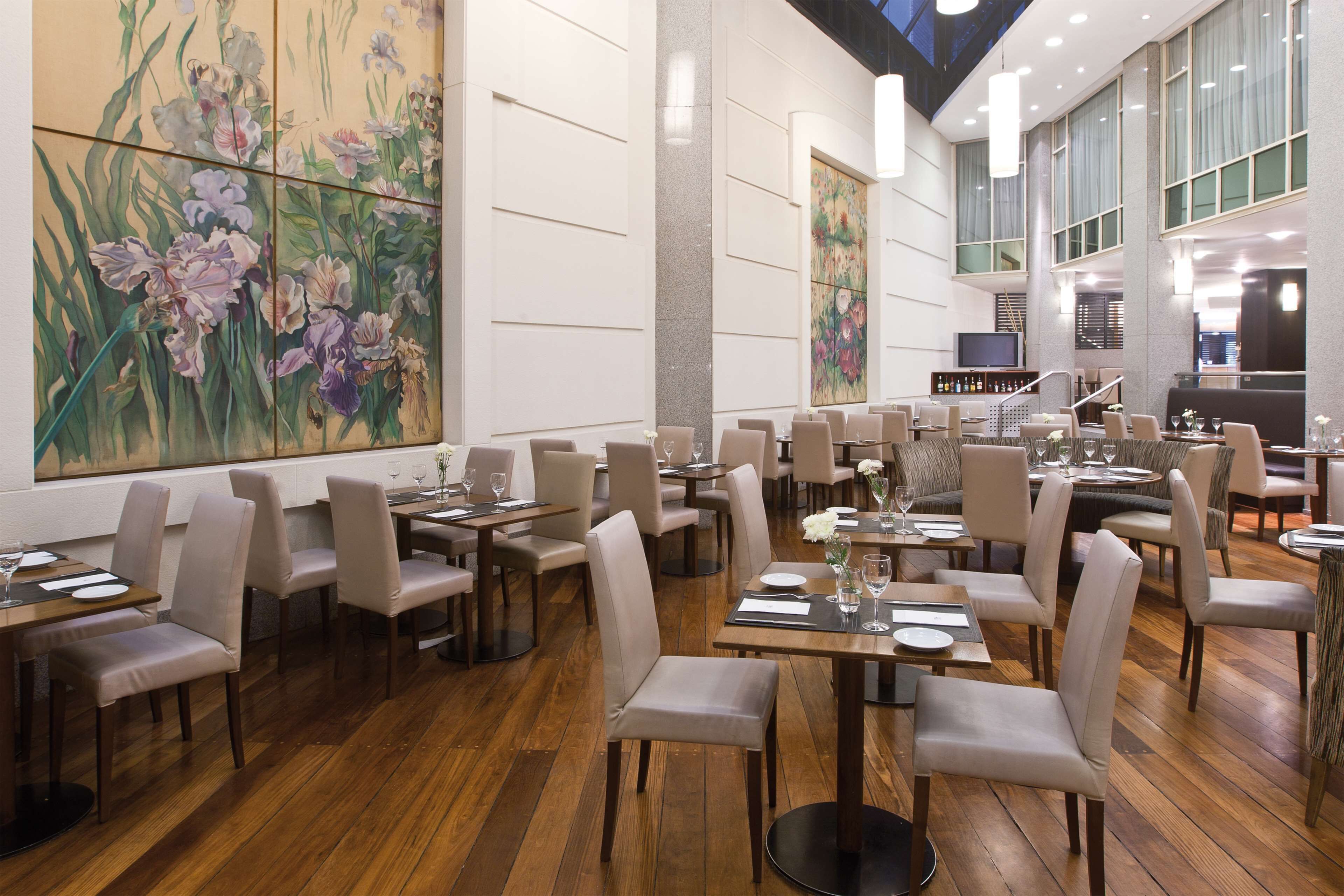 A spacious dining area with multiple tables and chairs, a large floral painting on the wall, and a modern interior design.