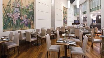 Uma sala de jantar espaçosa com várias mesas e cadeiras, um grande quadro floral na parede e um design de interiores moderno.