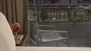 Quarto de hotel com varanda e vista para a paisagem urbana ao pôr do sol.