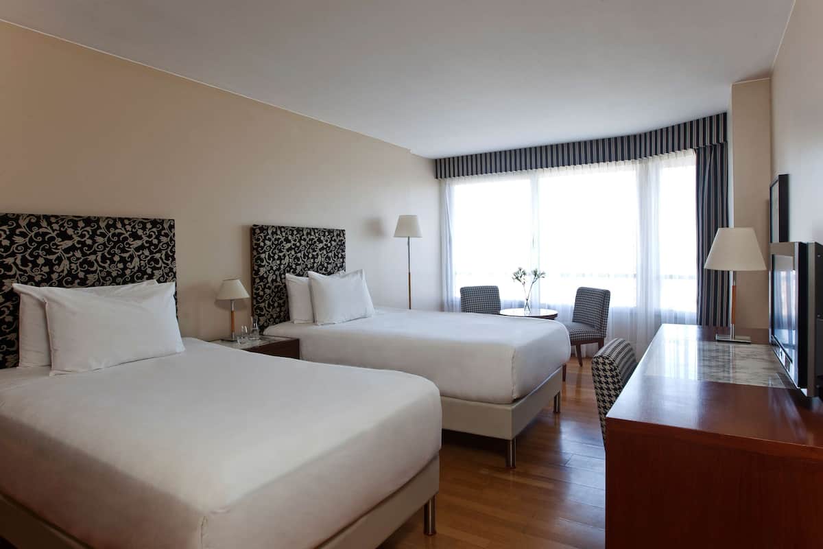 Une chambre d’hôtel avec deux lits, un bureau, une chaise et une télévision.