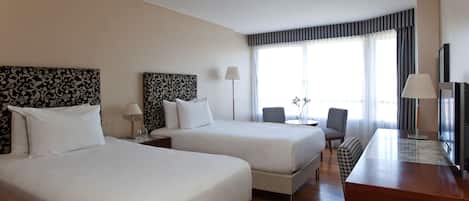 A hotel room with two beds, a desk, a chair, and a TV.