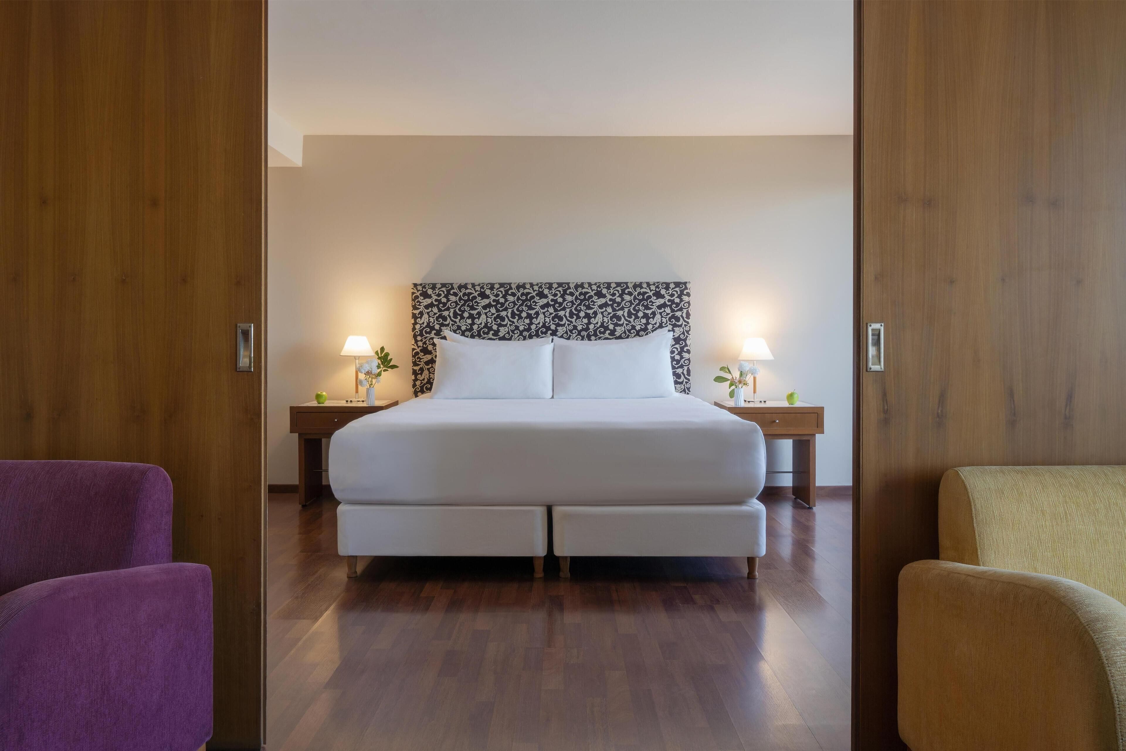 A neatly arranged bedroom with a large bed, two bedside tables with lamps, and a wooden floor.