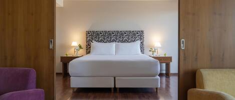 A neatly arranged bedroom with a large bed, two bedside tables with lamps, and a wooden floor.