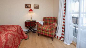 A room with a bed, a chair, a small table with a lamp, and two framed pictures on the wall.