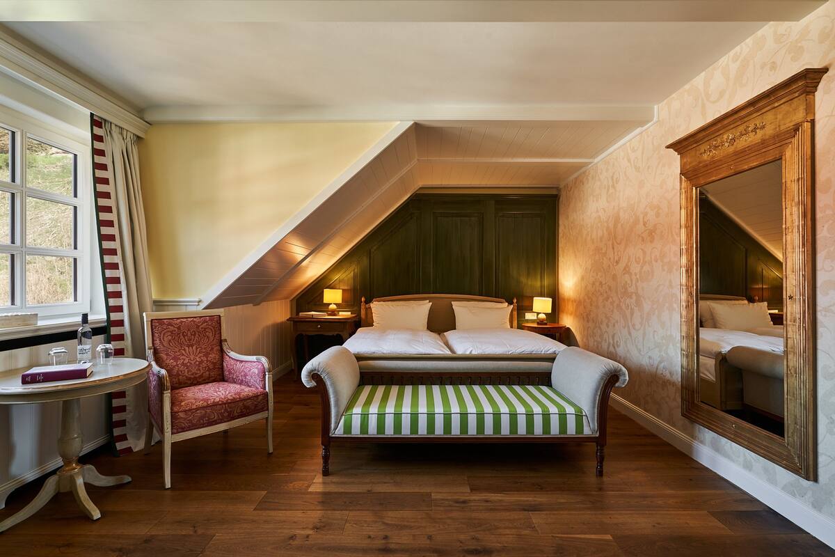 Een slaapkamer met een bed, een stoel, een tafel en een spiegel.