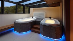 Ein modernes Badezimmer mit zwei separaten Whirlpools, einer eingebauten Heizung und Blick ins Freie durch große Fenster.