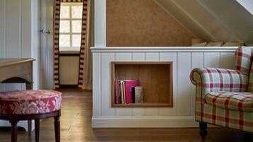 Una habitación con un banco de madera, un sillón escocés y una estantería empotrada llena de libros.