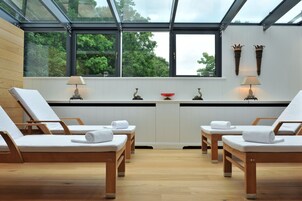Un cuarto de spa con sillas de madera y techo de cristal, que ofrece vistas al exterior de la vegetación.