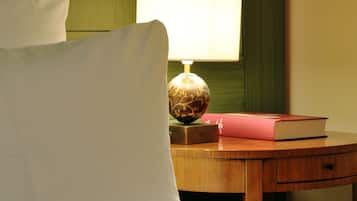 A neatly made bed with white linens, a wooden bedside table with a lamp and a book, and a green wall in the background.