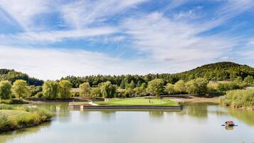 A serene landscape with a golf course, a calm lake, and a forested hill in the background.