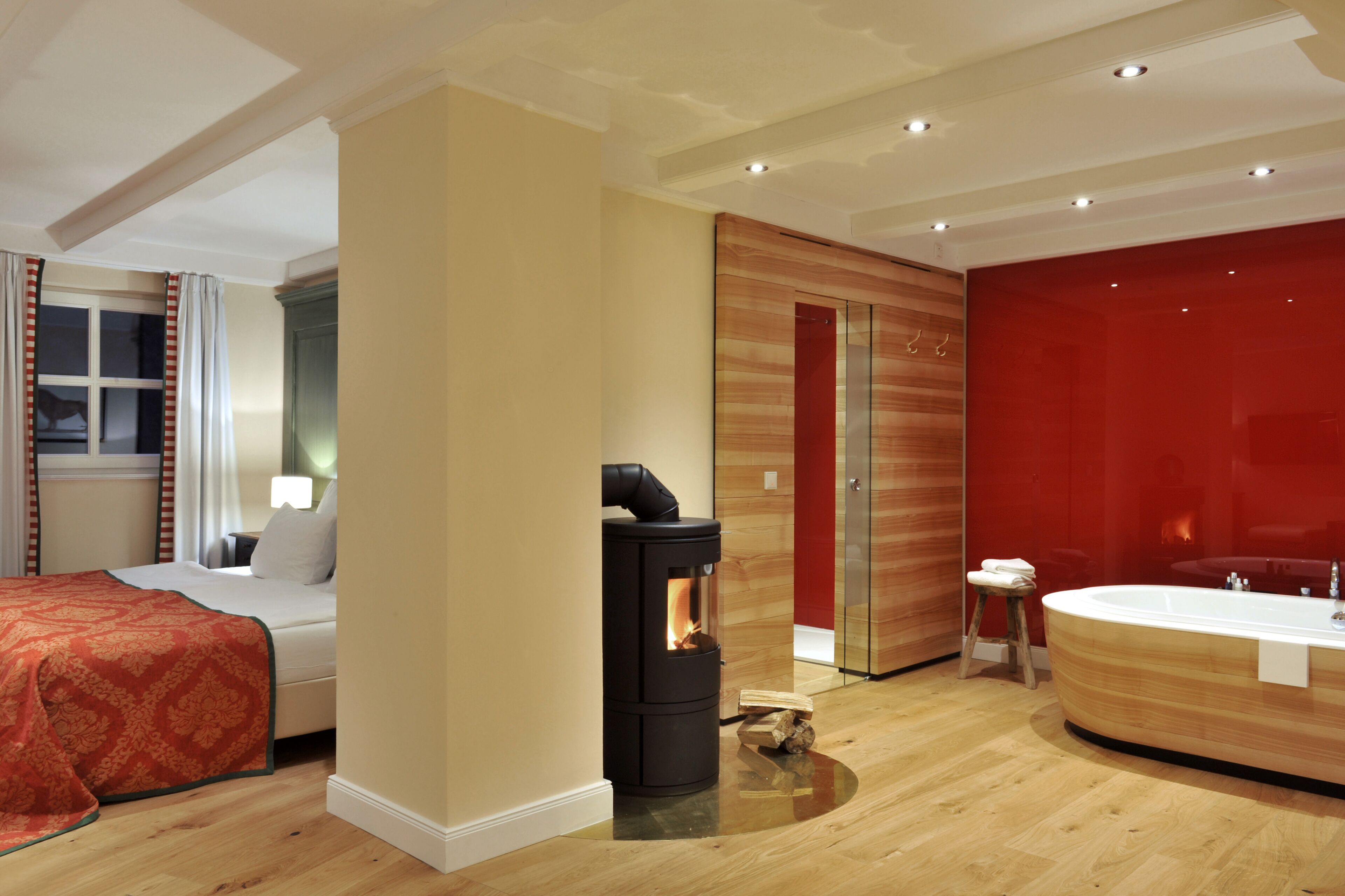 Ett modernt hotellrum med en säng, en vedeldad kamin, ett stort badkar och en vägg som är accentuerad med rött.