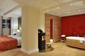 Habitació d'hotel moderna amb llit, una llar de fusta, una banyera gran i una paret d'accent vermella.